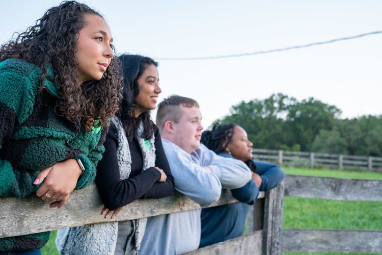 A diverse group of teens standing at a fence with their arms hanging over the rail.