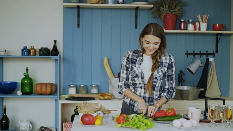 A young woman cutting fresh produce in a kitchen for use in a salad.