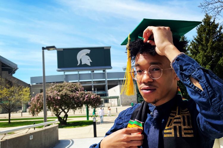 Evan Morton poses in front of Spartan Stadium in graduation cap and gown