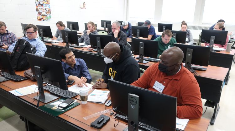 Ghane is kneeling on the floor by the computers where students sit