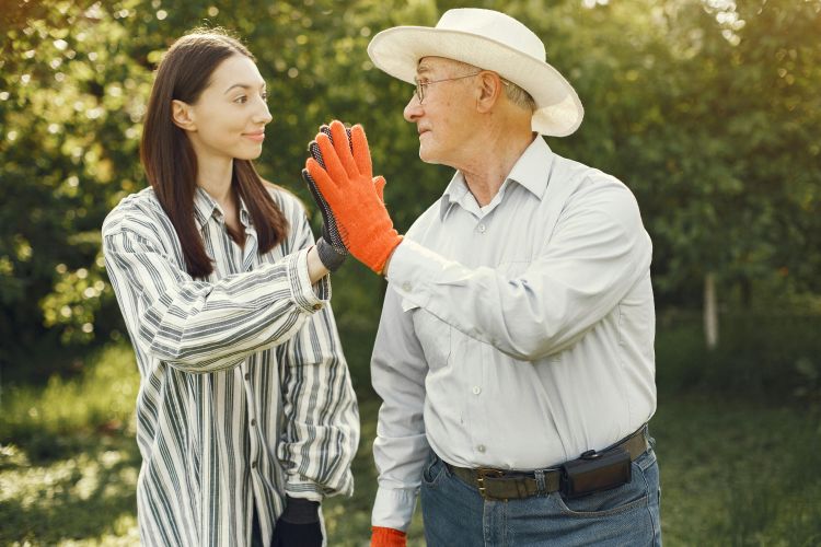 a young woman and older man give each other a high five in an orchard