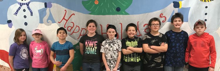 Smiling youth stand in front of a holiday banner.