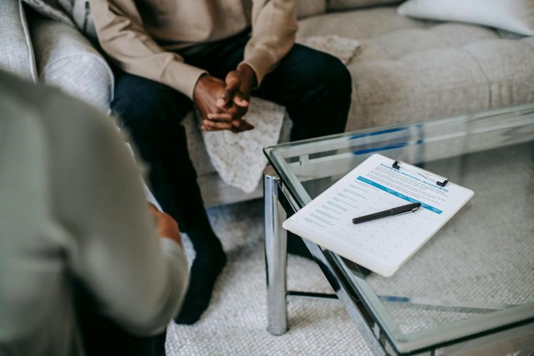 A photo of a therapy sessions between two people, no faces are shown, and there is a notepad and pen on the table.