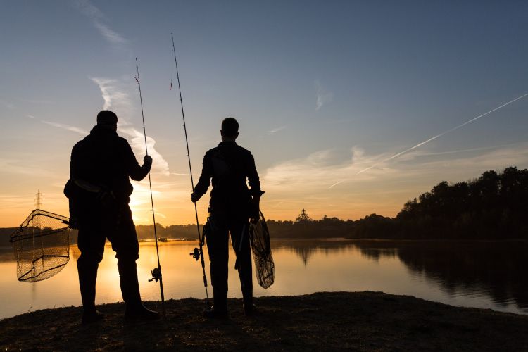 Two fisherman stand on the shore of a freshwater lake at sunrise