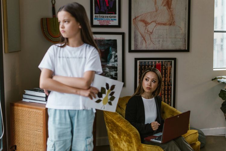 A child with her arms crossed looking away from a woman who is looking at her.