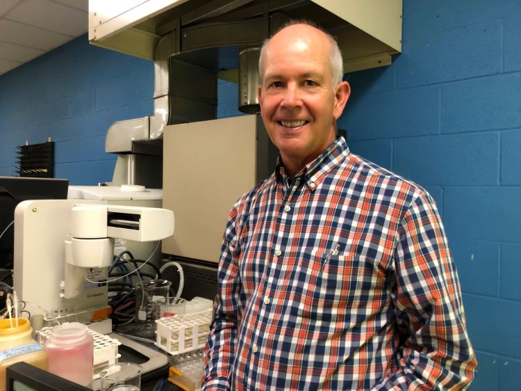 Jon Dahl smiling next to lab equipment.