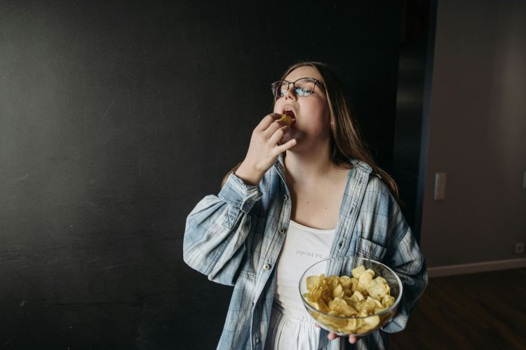 A photo of a young woman eating chips.