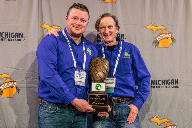 Two men standing together holding a trophy shaped like a hop plant.