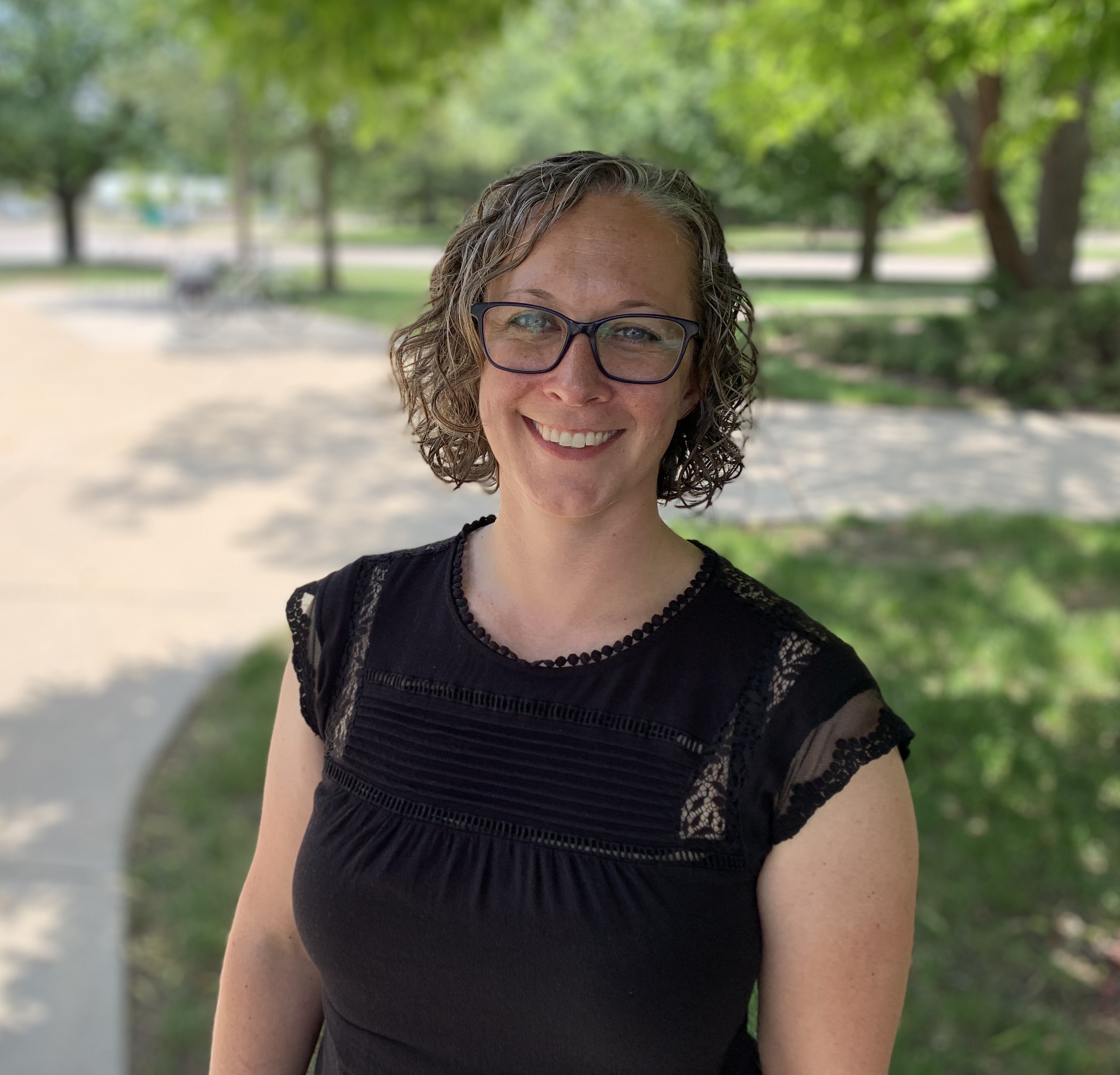 Outdoor portrait of Aislinn with green trees and grass in the background.