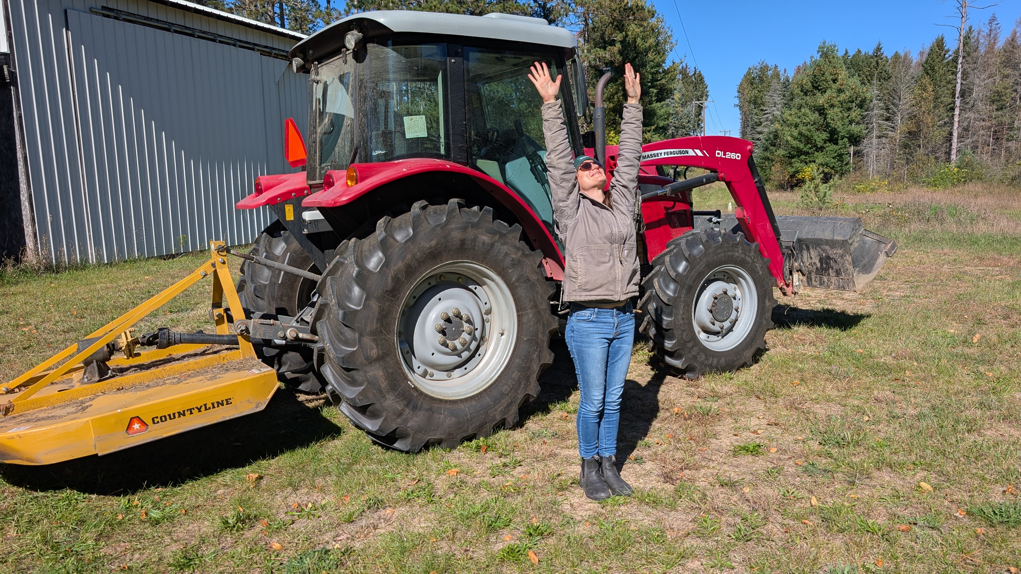 person standing in front of red tractor stretching arms in air