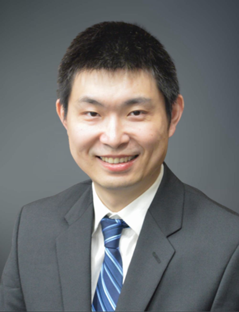 Studio headshot of Dong Zhao wearing a dark suit jacket, white dress shirt and blue striped tie, photographed against a neutral gray background with soft, even lighting.